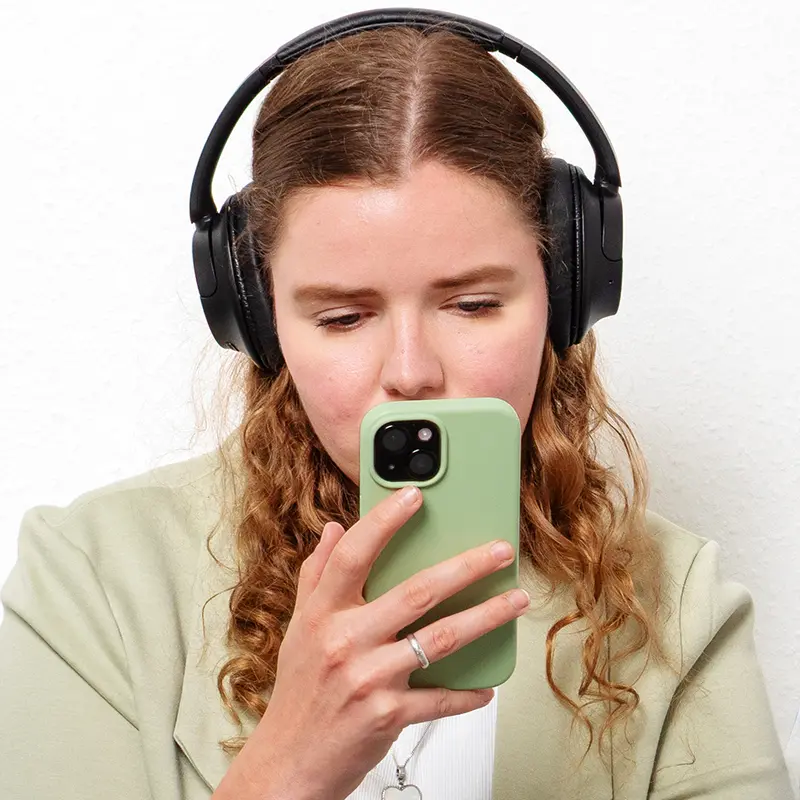 Frau mit langen, lockigen Haaren, die Kopfhörer trägt und ein Smartphone in der Hand hält.