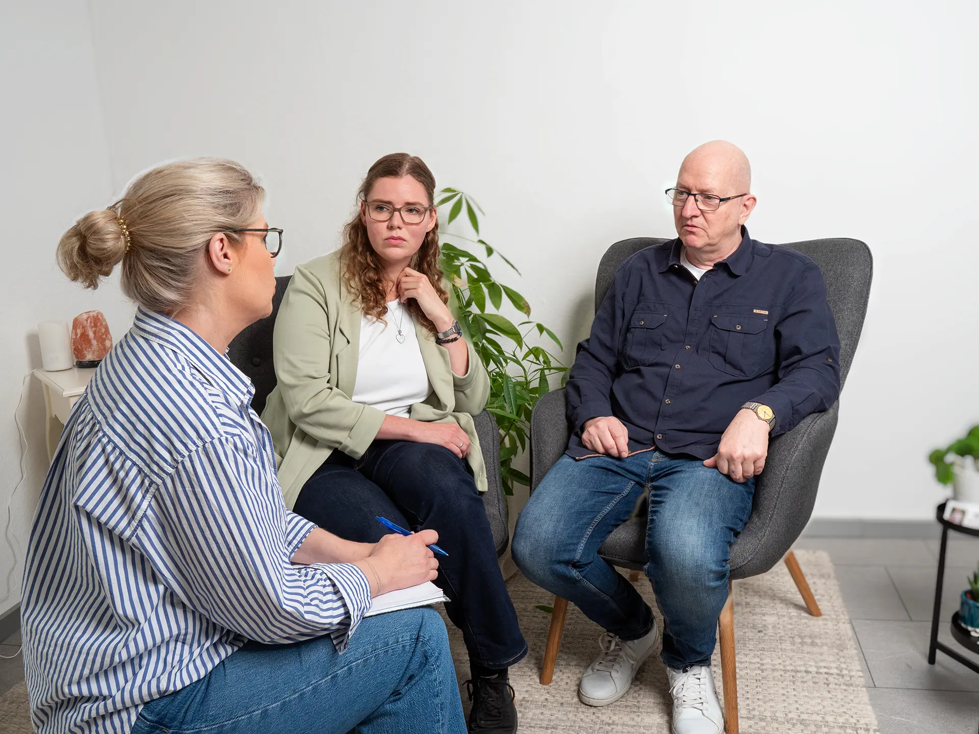 Drei Personen sitzen in einem Raum und führen ein Gespräch, eine Person notiert etwas.